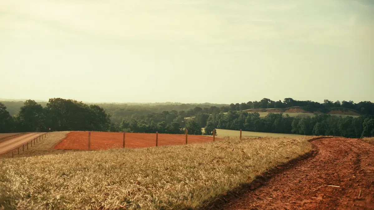 Cleared rural building site with a graded red clay pad and survey stakes on a North Alabama rise