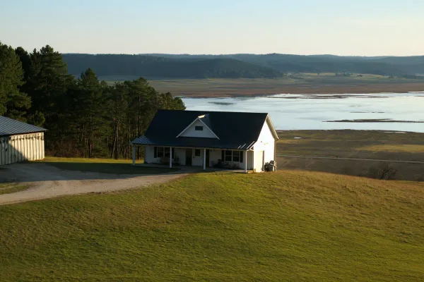 White barndominium with a black metal roof and porch on a hilltop above the lake near Centre in Cherokee County, Alabama
