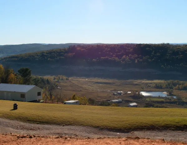 Post-frame home on a hillside lot in a valley of small farms below a forested ridge in St. Clair County, Alabama