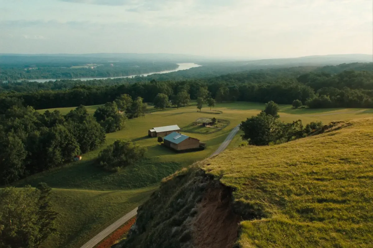 North Alabama plateau farms and metal-roofed homes above a hazy river valley seen from a sandstone bluff