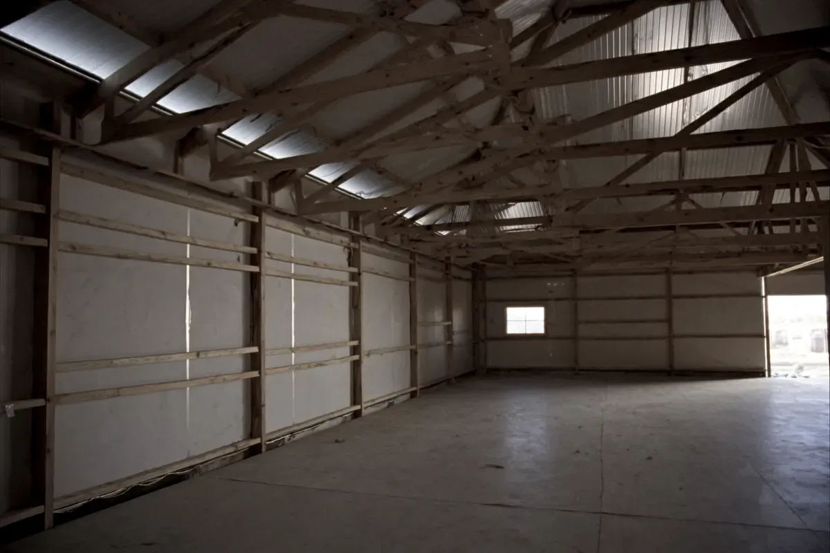 Interior of a dried-in post-frame home shell with wood columns, girts and trusses over a concrete slab