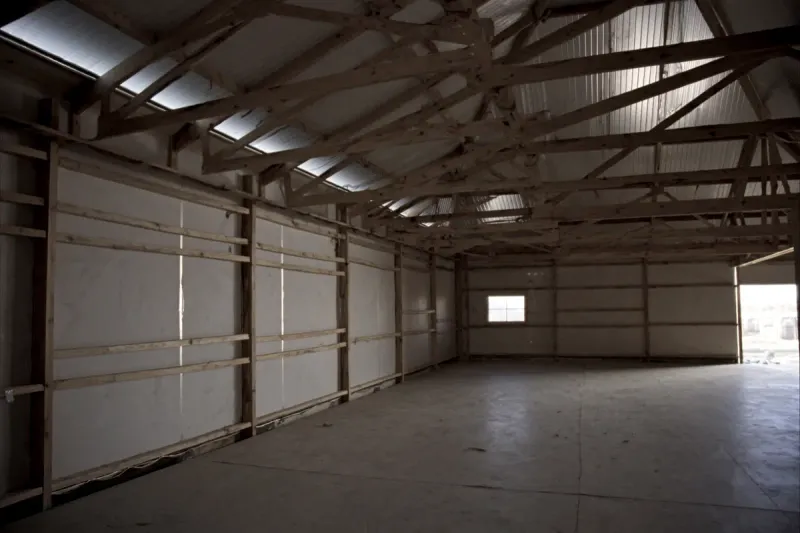 Interior of a dried-in post-frame home shell with wood columns, girts and trusses over a concrete slab