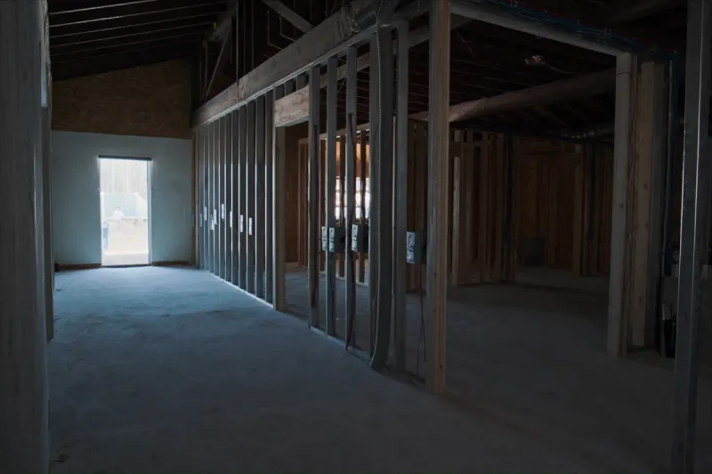 Barndominium interior at the rough-in stage with framed stud walls, electrical boxes and conduit inside a post-frame shell
