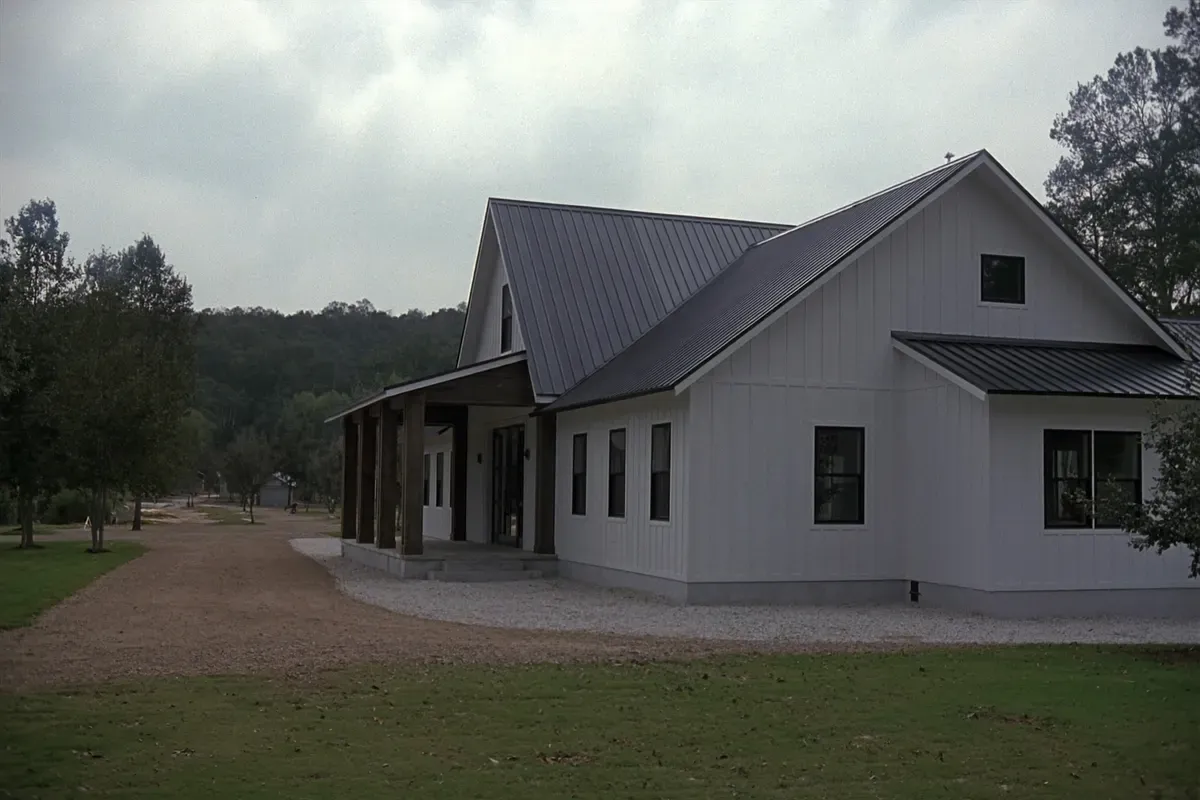 Finished white board-and-batten post-frame barndominium with a charcoal metal roof and covered porch in North Alabama
